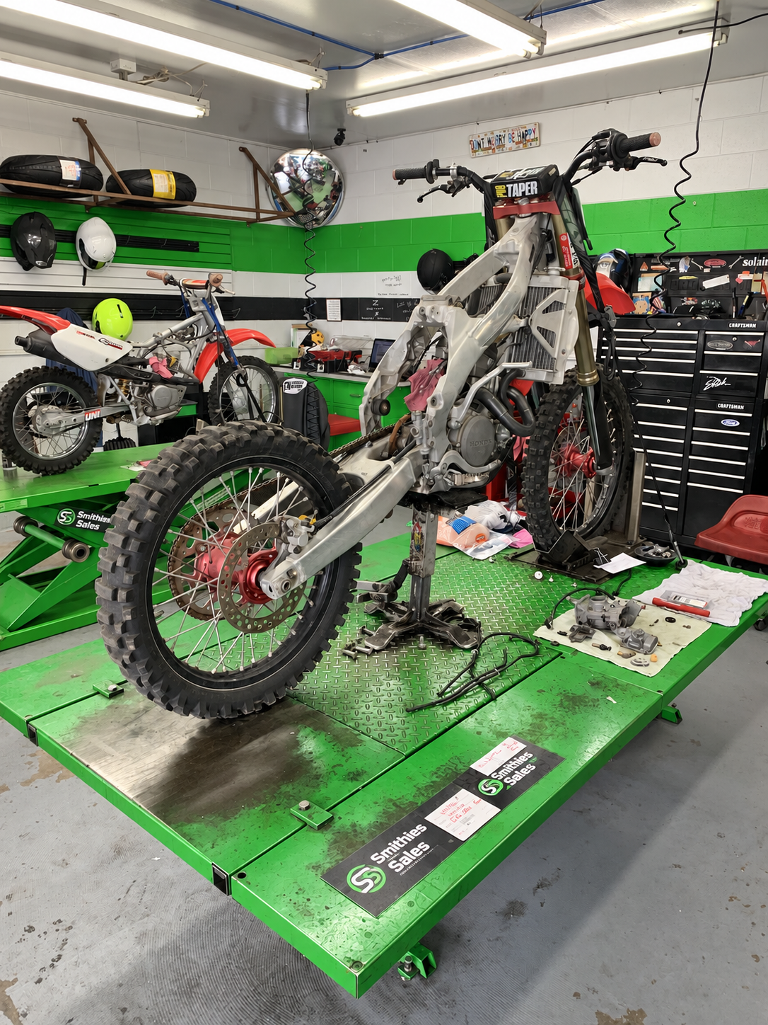 A motocross bike being repaired on a green Smithies Sales workshop lift